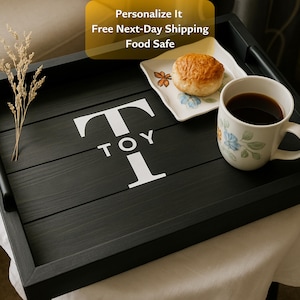 May include: A black wooden serving tray with the word "TOY" and the letter "T" in white. The tray holds a mug of coffee, a roll, and a small plate. The tray has handles and is food safe.