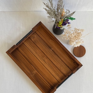 May include: A rectangular wooden tray with black metal handles. The tray has a natural wood finish and is made of wood planks.