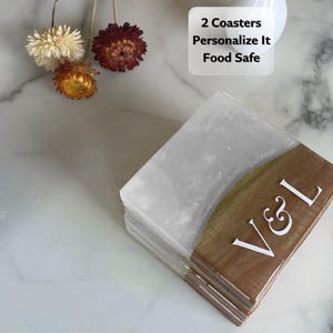 May include: A stack of two square coasters. The top half of each coaster is a translucent white, and the bottom half is a brown wood grain. White letters "V & L" are on the wood grain. Text on the image reads "2 Coasters Personalize It Food Safe."