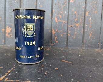 May include: A vintage blue metal cylinder with the text "SEXENNIAL REUNION" and "1934" in gold lettering. The cylinder also features a crest and the date "JUNE 15-19. 1940". The cylinder has a dark rim and is slightly worn.