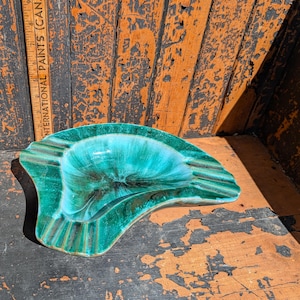 May include: A vintage, turquoise ashtray with a unique, organic shape. The ashtray has a glossy finish with dark brown accents and a ridged design on the side. The ashtray is approximately 20 cm long.