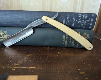May include: A vintage straight razor with a white plastic handle. The razor blade is engraved with the words "My Secret".