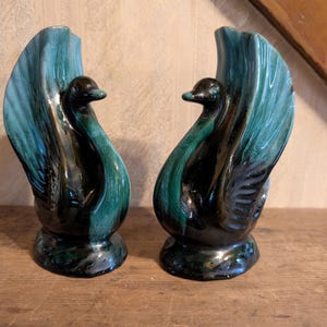 Puede incluir: Par de jarrones de cisne de cerámica vintage. Cada jarrón presenta un diseño de cisne con una combinación de colores verde azulado y negro. Los jarrones tienen un acabado brillante y se exhiben sobre una superficie de madera. Decoración del hogar.