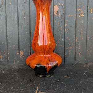 May include: A tall, decorative vase with a glossy finish. The vase features a striking color gradient, transitioning from a dark brown top to a vibrant orange center and a black base. The vase has a bulbous midsection and a slender neck.