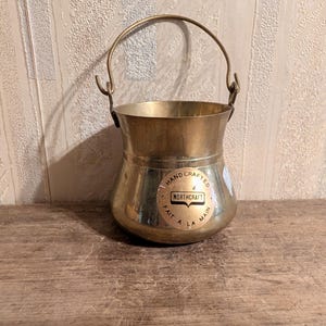 Peut inclure: Un petit seau de couleur laiton avec une poignée incurvée. Le seau a une base arrondie et un dessus plus large. Un autocollant circulaire sur le devant indique "HAND CRAFTED NORTHCRAFT FAIT A LA MAIN."