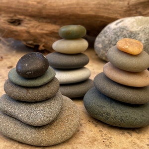 May include: Three stacks of smooth, gray and brown stones, each balanced on top of the other. The stones are arranged in a pyramid shape, with the top stone being the smallest.