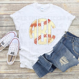 Op de afbeelding: Wit T-shirt met een baseball-thema monogram ontwerp met de letters "ABC" in een cirkel. De baseball is verweerd en heeft rode naden.