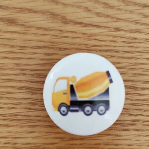 Op de afbeelding: Een ronde witte knop met een illustratie van een gele en zwarte betonmixer.