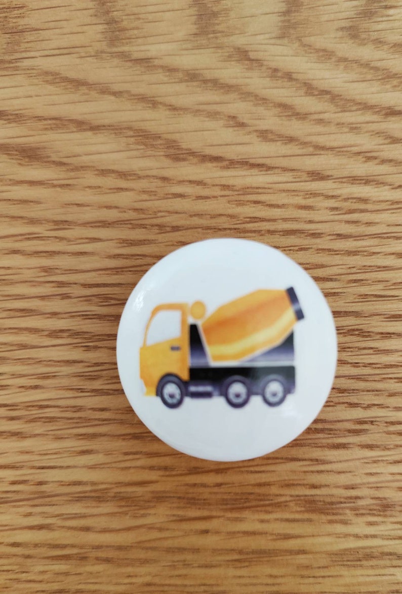 Op de afbeelding: Een ronde witte knop met een illustratie van een gele en zwarte betonmixer.