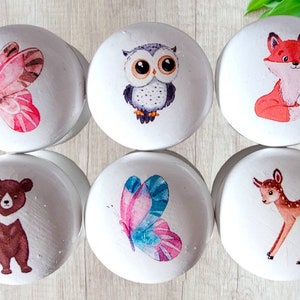 May include: Set of six white wooden cabinet knobs with colorful illustrations of woodland creatures and butterflies. Designs include a butterfly, owl, fox, bear, butterfly, and deer. These knobs are perfect for adding a whimsical touch to furniture.