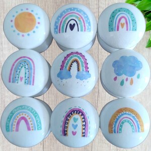 May include: Set of ten ceramic knobs with rainbow designs. The knobs feature different rainbow designs, including a sun, clouds, and hearts. The knobs are white with colourful designs.