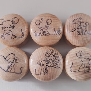 May include: Six wooden round ornaments with different designs featuring a mouse holding a flower, a heart, a sunflower, and a tulip. Each ornament has a black and white line drawing of a mouse.