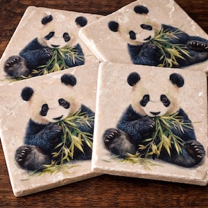 May include: Four square stone coasters with a panda bear design. Each coaster features a panda bear with black and white fur, eating bamboo leaves. The coasters have a beige background with a marble-like texture.