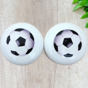 May include: Two white ceramic knobs with a black and white football design.