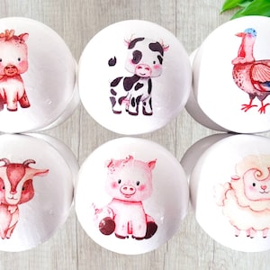 Peut inclure: Six boutons ronds en bois blanc avec des illustrations de différents animaux de la ferme. Les animaux sont un cochon, une vache, une chèvre, une dinde, un mouton et un cheval. Les boutons sont peints avec des détails ressemblant à de l'aquarelle.