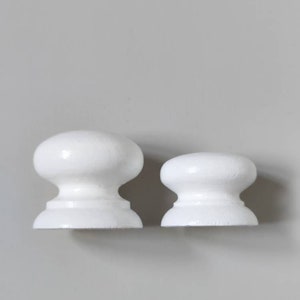 Op de afbeelding: Twee witte keramische knoppen, een groter dan de andere, met een afgeronde bovenkant en een platte basis.