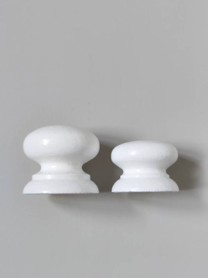 Op de afbeelding: Twee witte keramische knoppen, een groter dan de andere, met een afgeronde bovenkant en een platte basis.
