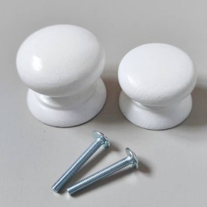 Op de afbeelding: Twee witte houten knoppen met zilveren schroeven. De knoppen zijn rond en hebben een gladde afwerking.