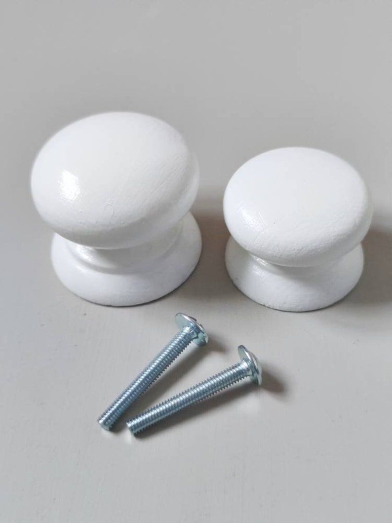 Op de afbeelding: Twee witte houten knoppen met zilveren schroeven. De knoppen zijn rond en hebben een gladde afwerking.