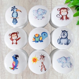 May include: Nine white ceramic knobs with colorful animal illustrations. The animals include a toucan, elephant, monkey, turtle, rhinoceros, parrot, giraffe, and two elephants.