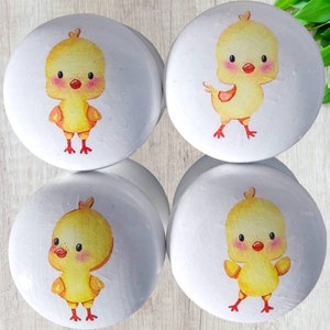 Puede incluir: Cuatro pomos redondos blancos con pollitos amarillos pintados en ellos. Los pollitos tienen picos y patas rojas.