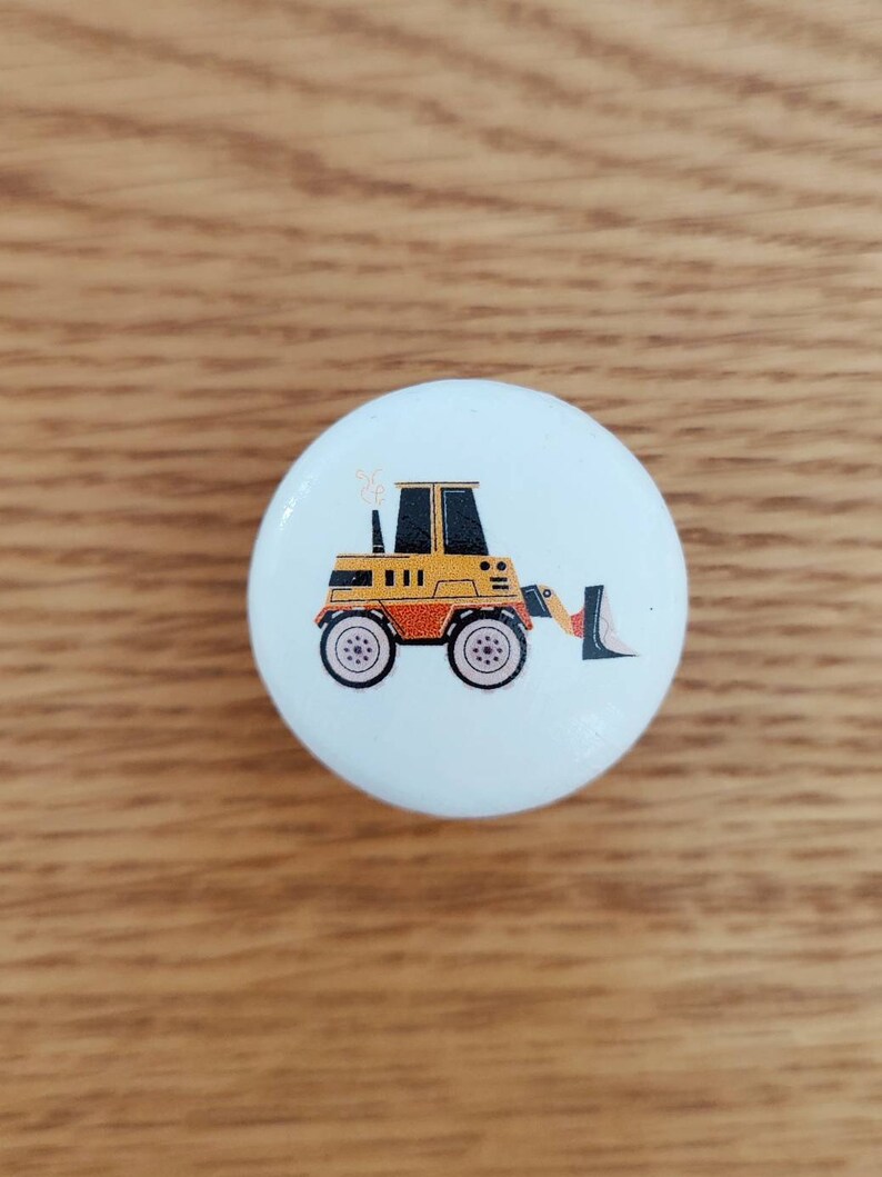 Op de afbeelding: Een witte keramische knop met een ontwerp van een gele en zwarte cartoon-graafmachine.