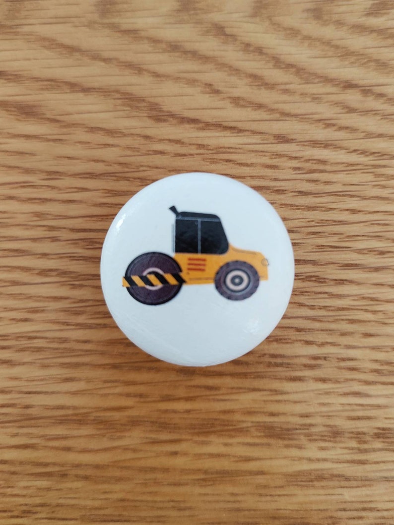 Op de afbeelding: Een knoop met een geel en zwart bouwvoertuig. Het voertuig heeft een zwarte cabine en een grote gele rol.