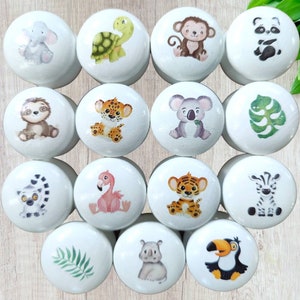 Könnte beinhalten: Set mit 15 weißen Keramik-Knöpfen mit verschiedenen Tier- und Naturmotiven. Die Motive umfassen ein Faultier, einen Tiger, einen Koala, ein Zebra, einen Flamingo, einen Tukan, einen Lemur, eine Schildkröte, einen Affen, einen Panda, ein Flusspferd, ein Blatt und einen Tiger.