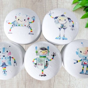 May include: Five white, round cabinet knobs with colorful robot designs. Each robot has a unique design with rainbow accents, and they are smiling. These knobs are perfect for a child's room or a playful decor.