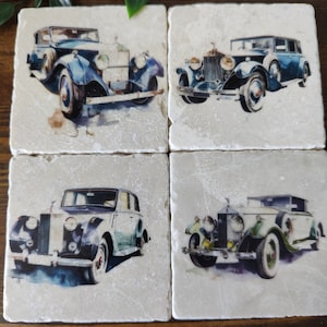 May include: Set of four square coasters featuring vintage cars. Each coaster has a different car, all in shades of blue, green, and white. The coasters are made of marble and have a white background.