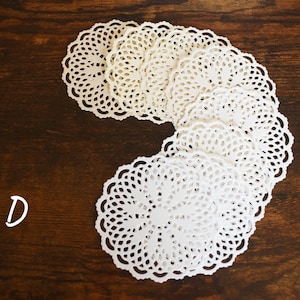May include: A stack of white paper doilies with a scalloped edge, arranged in a C shape on a brown wooden surface. The letter D is written in white on the wood.