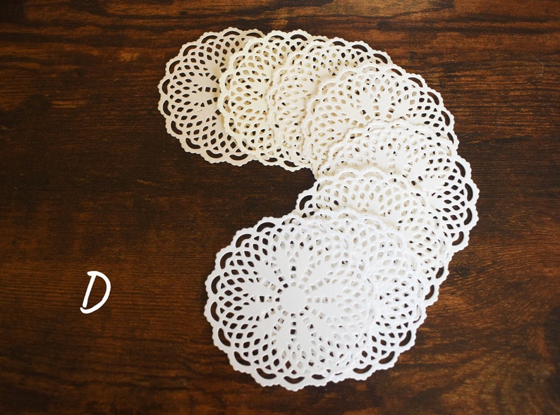 May include: A stack of white paper doilies with a scalloped edge, arranged in a C shape on a brown wooden surface. The letter D is written in white on the wood.