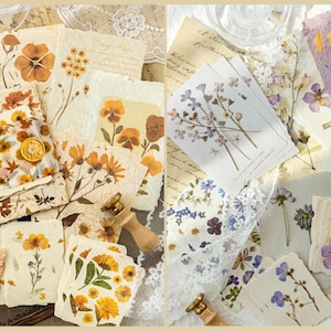 May include: A collection of handmade paper and cards featuring pressed flowers in shades of yellow, orange, and purple. The paper has a rustic, vintage aesthetic, with some pieces bearing floral designs and handwritten text.