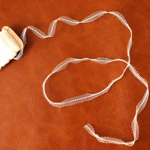 May include: A spool of white lace trim with a scalloped edge. The lace is on a brown surface.