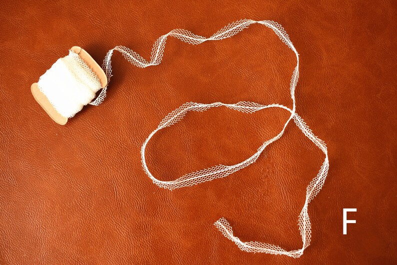 May include: A spool of white lace trim with a scalloped edge. The lace is on a brown surface.