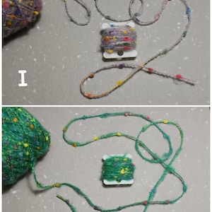 Puede incluir: Dos carretes de hilo de colores con peque&ntilde;as cuentas tejidas en el hilo. El hilo est&aacute; enrollado alrededor de un carrete de pl&aacute;stico blanco. El hilo del carrete superior es de color morado claro con cuentas multicolores. El hilo del carrete inferior es de color verde con cuentas multicolores.