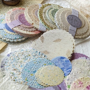 May include: A selection of decorative paper circles in diverse colours and textures. Some circles feature floral patterns, while others have script or leaf designs. Bundles are tied with ribbons, creating a vintage and artistic aesthetic.