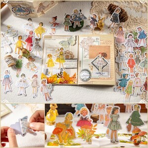 May include: A sheet of vintage-style stickers featuring illustrations of girls in various dresses. The stickers are printed on white paper with a glossy finish. The stickers are perfect for scrapbooking, journaling, and other craft projects.