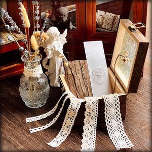 Puede incluir: Una caja de madera con tapa abatible, decorada con un patrón floral. La caja está abierta y contiene un trozo de madera, una tarjeta con el texto "The Vintage Label" y varios trozos de encaje blanco.