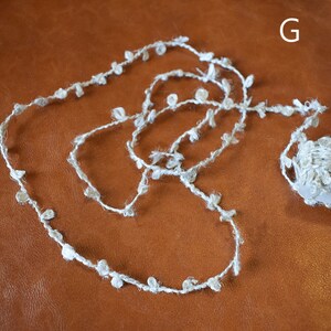 May include: A roll of white yarn with small white pom-poms attached. The yarn is on a brown surface.