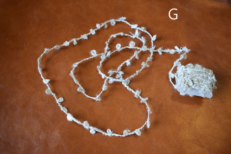 May include: A roll of white yarn with small white pom-poms attached. The yarn is on a brown surface.