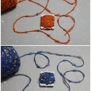 Puede incluir: Dos carretes de hilo, uno naranja y otro azul, con motas de colores por todas partes. Cada carrete est&aacute; enrollado con una longitud de hilo, y el hilo est&aacute; dispuesto en un bucle suelto.