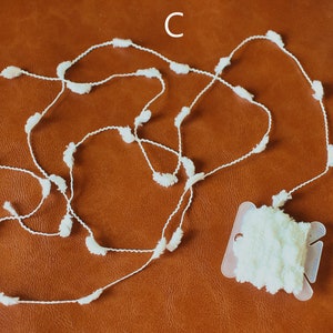 May include: A white pom-pom trim with a spool of the trim. The trim is made of a thin white string with small white pom-poms attached to it.