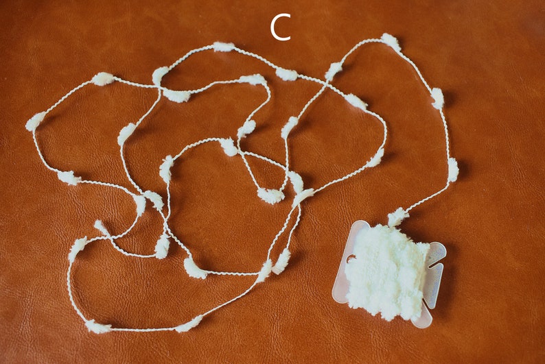 May include: A white pom-pom trim with a spool of the trim. The trim is made of a thin white string with small white pom-poms attached to it.