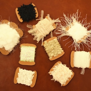 Könnte beinhalten: Sortiment aus zehn Spulen mit weißer, schwarzer und beigefarbener Spitzenborte, auf braunem Karton präsentiert.