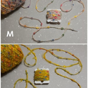 Puede incluir: Dos ovillos de hilo, uno beige y otro amarillo, con motas de colores. Cada ovillo est&aacute; enrollado alrededor de un centro de cart&oacute;n y tiene un peque&ntilde;o ovillo de hilo colorido enrollado que est&aacute; unido a &eacute;l. Los ovillos est&aacute;n etiquetados como "M" y "N".