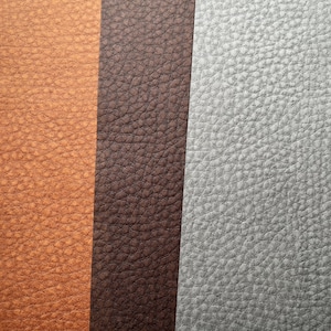 May include: Close-up of various textured leather swatches in shades of tan, brown, and gray. The leather has a pebbled grain, and the colors vary from light to dark.