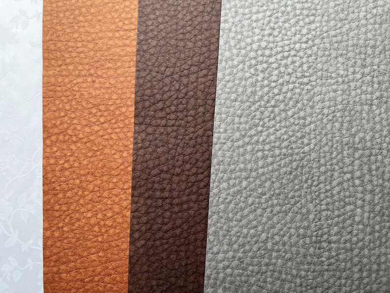 May include: Close-up of various textured leather swatches in shades of tan, brown, and gray. The leather has a pebbled grain, and the colors vary from light to dark.