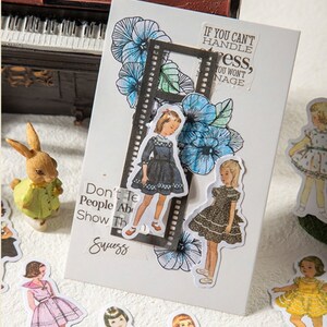 May include: A set of vintage-style stickers featuring illustrations of girls wearing dresses. The stickers are on a white background with a black and white film strip border. The text "If you can't handle stress, you won't manage" is on the sticker sheet.