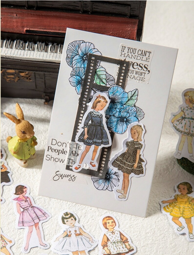 May include: A set of vintage-style stickers featuring illustrations of girls wearing dresses. The stickers are on a white background with a black and white film strip border. The text "If you can't handle stress, you won't manage" is on the sticker sheet.